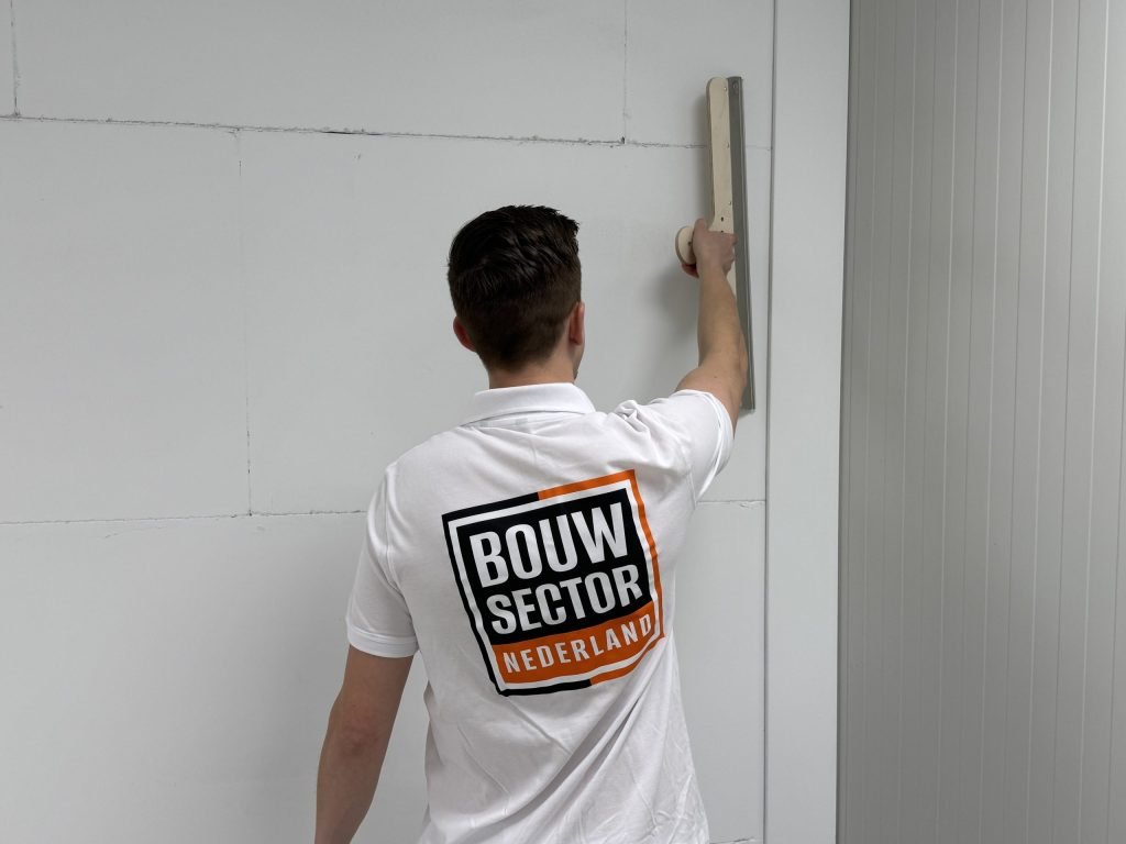 Achteraanzicht van een stukadoor van Bouwsector Nederland die een spaan hoog langs een wand haalt