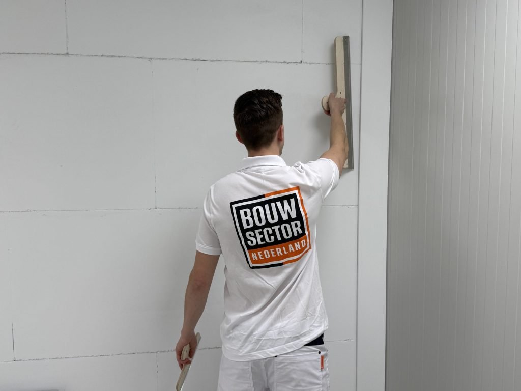 Stukadoor strekt zijn arm en trekt de spaan over het bovenste deel van een lichte wand