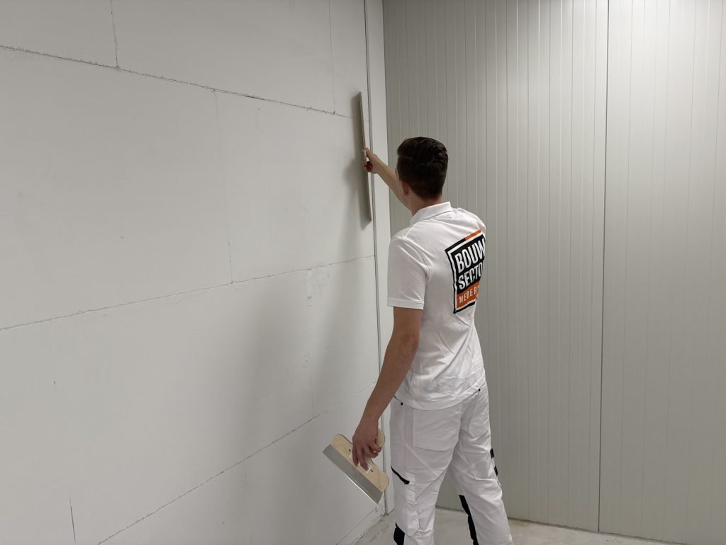 Stukadoor houdt een spaan verticaal langs de hoek van een wand met zichtbare naden